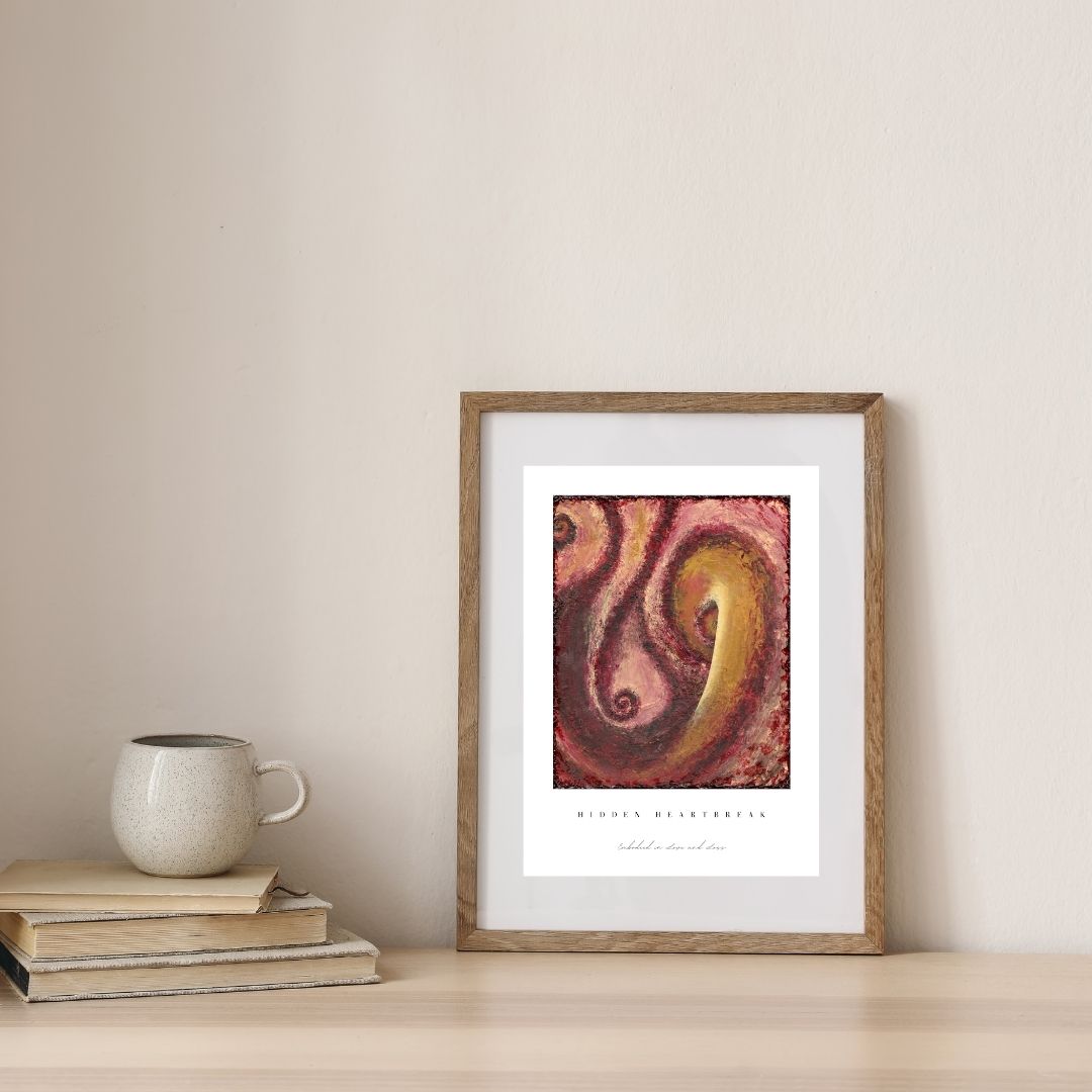 Framed abstract art print on a table with books and a mug.