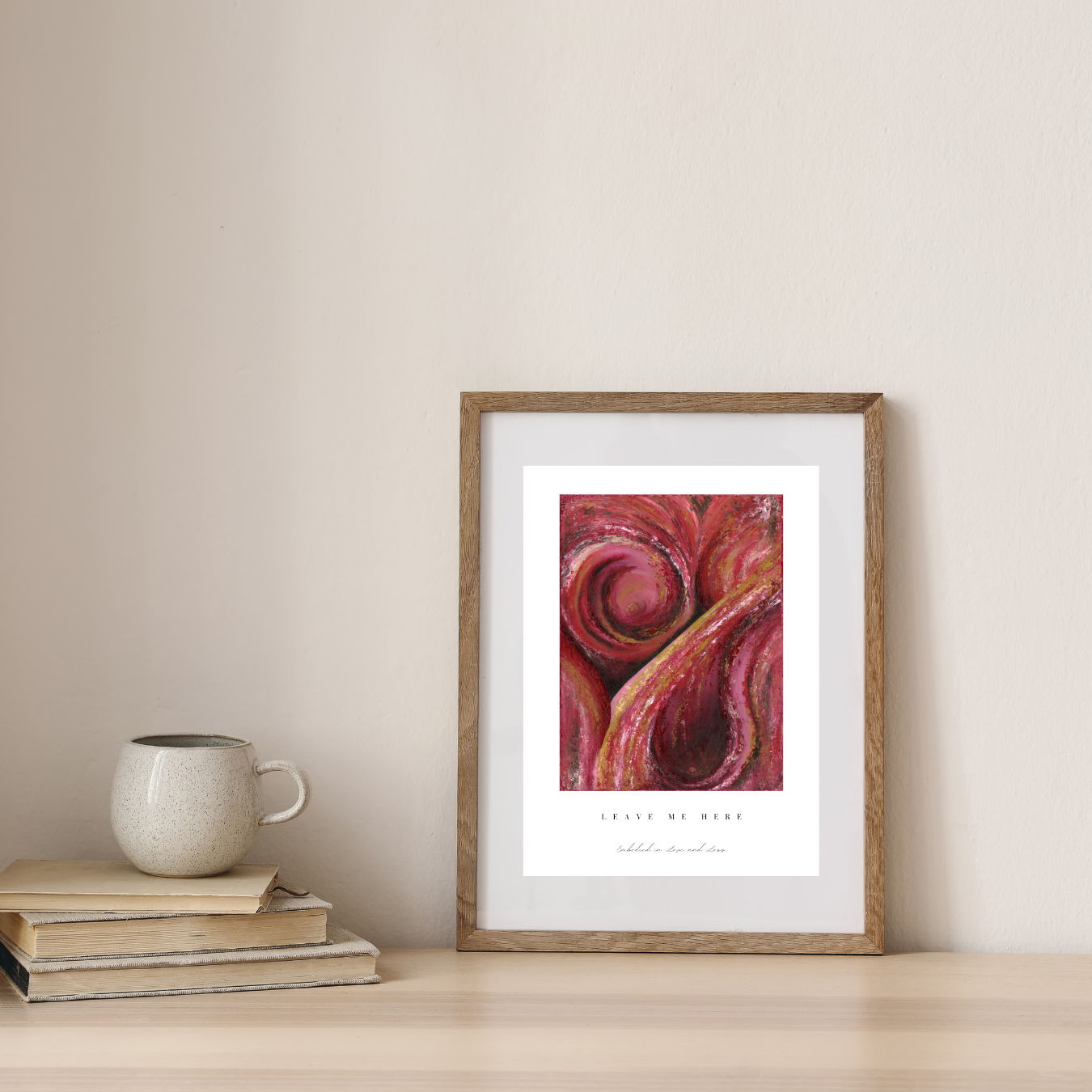 Framed abstract art print on a wall with books and a mug below