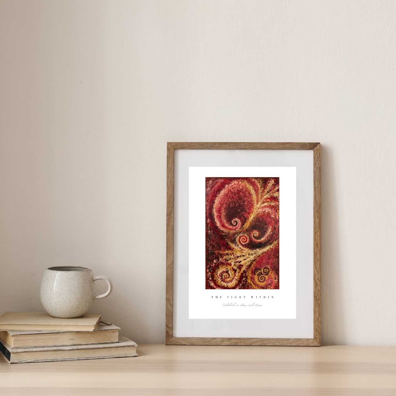 Framed artwork with a swirling design on a neutral wall with books and a mug.