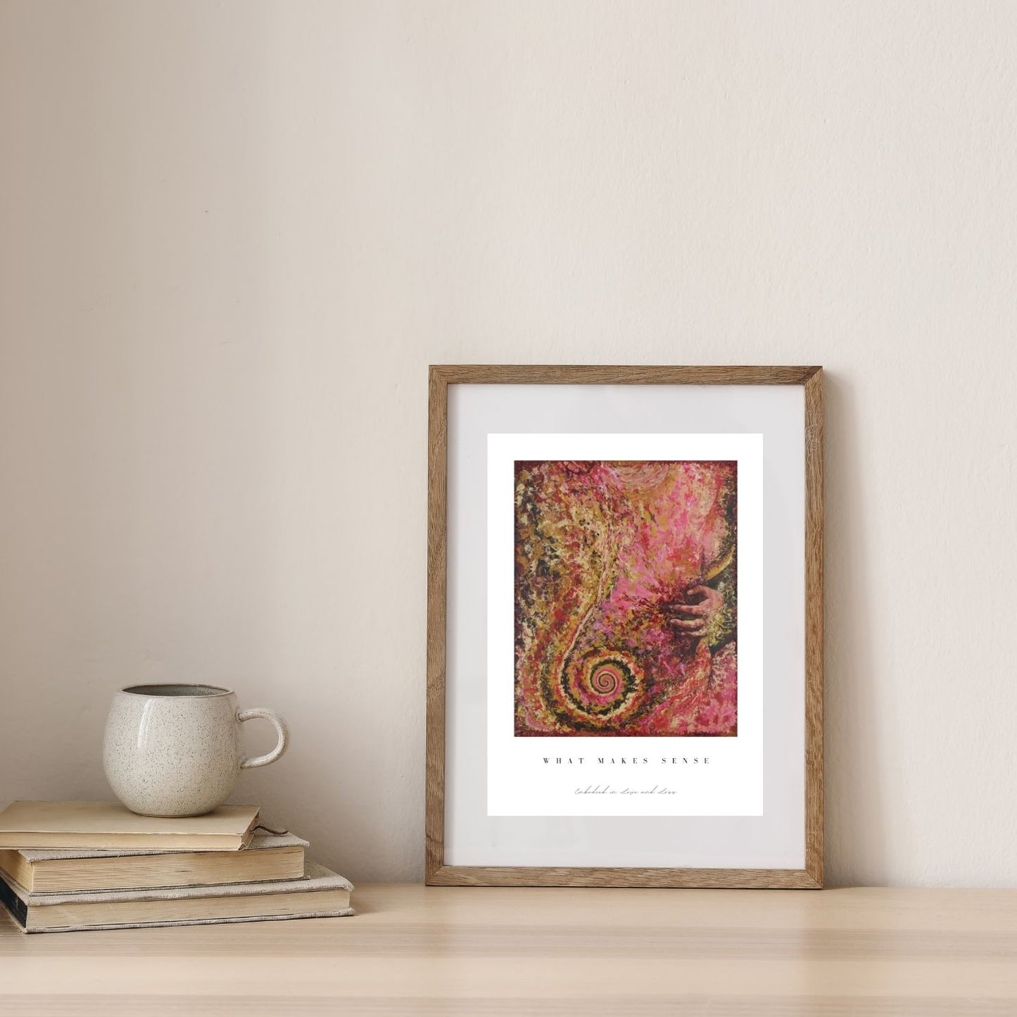Framed abstract art print on a wall with books and a mug below